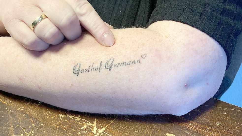 Katja Scherler zeigt auf ihr Tattoo mit dem Namen des Gasthofes.