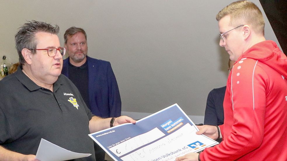 Jeweils 8000 Euro für vier Sportvereine: Lotterie-Chef Jens Coordes (links) übergibt hier André Schoon vom VfB Germania Wiesmoor einen Riesen-Scheck. Im Hintergrund verfolgt KV-Chef Udo Hippen die Spendenübergabe. Foto: Romuald Banik