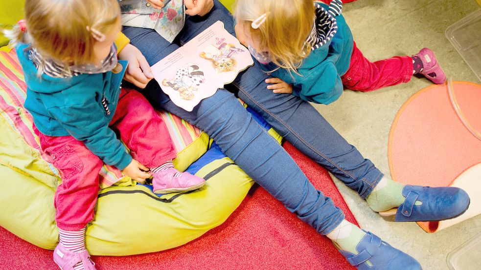 Eine Erzieherin liest mit Zwillingen ein Buch. Foto: Julian Stratenschulte/DPA