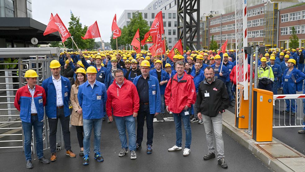 Mitarbeiter der Werft stehen mit Fahnen der IG Metall unmittelbar nach der Betriebsversammlung an einem Werkstor. Foto: Lars Penning/DPA