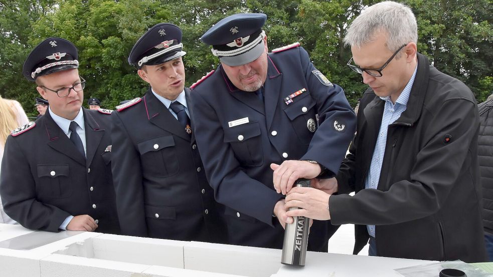 Mit vereinten Kräften füllten die Feuerwehrchefs Tobias Dirks (von links), Erhard Tammen und Klaus Dieter Cassens und Vize-Verwaltungschef Jochen Behrends die kurz darauf eingemauerte Zeitkapsel. Foto: Thomas Dirks