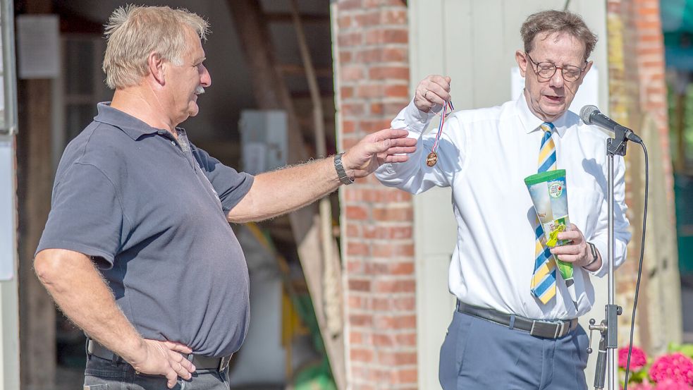Leezdorfs Pastor Peter Riesebeck (rechts) überreicht dem Heimatvereinsvorsitzenden Gerke Hugen (links) eine kleine Schultüte. Darin eine Goldmedaille für Hugens jahreslanges Engagement. Foto: Folkert Bents