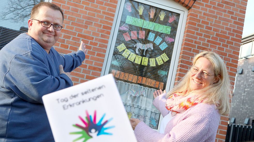 Als Werbung für den „Tag der seltenen Erkrankungen“ am 1. März hat Harm Mouson das Fenster seines Wohnzimmers bunt beklebt. Sandra Lotz-Kappelhoff vom Paritätischen Wohlfahrtsverband im Landkreis Aurich unterstützt sein Engagement und weiß um die Bedeutung von Austausch in Selbsthilfegruppen. Foto: Romuald Banik