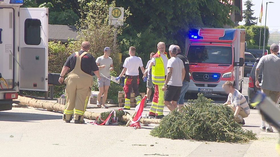 Der umgestürzte Maibaum liegt auf der Straße vor einem Einsatzwagen der Feuerwehr. Foto: Guido Schulmann/TV-Niederrhein/dpa