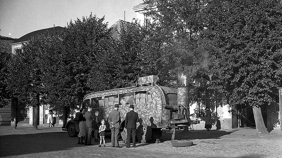 Mit Dampf wird dieser öffentliche Bus in Aurich betrieben. Die Aufnahme entstand Ende August 1945. Der Fahrer ist ausgestiegen, um einen Reifen zu wechseln, währen die Passagiere zuschauen. Foto: © Library and Archives Canada
