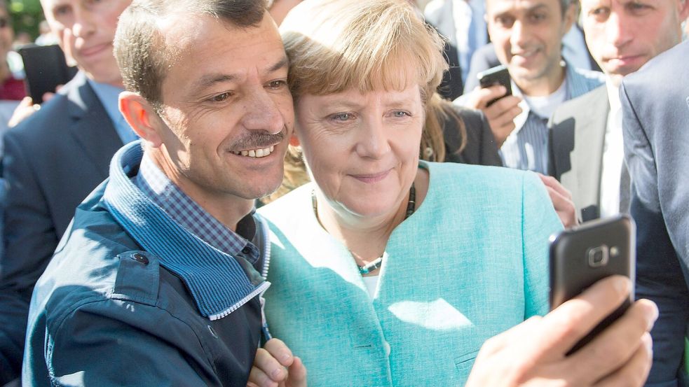 Bald zehn Jahre her: Angela Merkel (CDU) lässt sich nach dem Besuch einer Erstaufnahmeeinrichtung für Asylbewerber in Berlin-Spandau für ein Selfie zusammen mit einem Flüchtling fotografieren. (Archivbild) Foto: Bernd von Jutrczenka/dpa