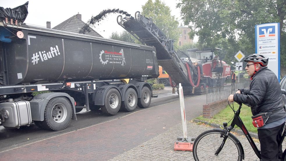 Eine tonnenschwere Fräse raspelt den alten Asphaltbelag der Kirchstraße in Marienhafe ab und befördert ihn auf einen vorausfahrenden Lastwagen, der das Fräsgut zur Wiederverwertung transportiert. Foto: Thomas Dirks