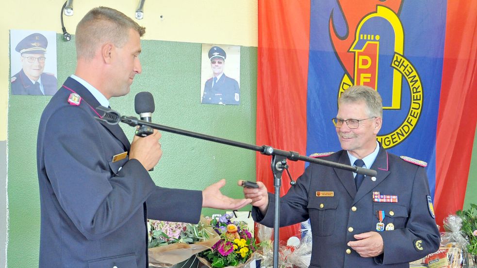 Ortsbrandmeister Dietmar Helmers verabschiedete seinen Vater vom aktiven Dienst und nahm ihn mit der symbolischen Abgabe des Funkmeldeempfängers in die Alters- und Ehrenabteilung der Feuerwehr Neßmersiel auf. Foto: Feuerwehrverband Ostfriesland