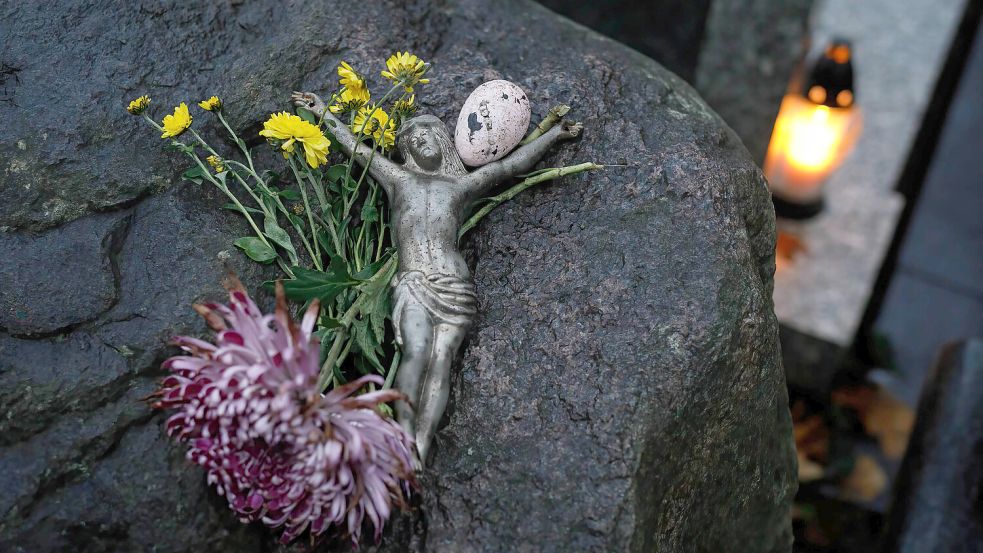 Ein Fragment einer Grabdekoration mit einer Christusfigur liegt neben einem Grablicht auf einem Grab. Kirchliche Berufe haben auch traurige Seiten. Foto: DPA