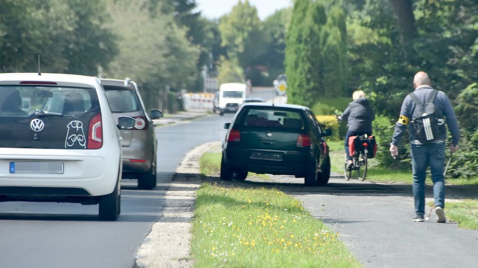 Eine Radfahrerin passiert den stillgelegten VW Golf, der seit Tagenden den Fuß- und Radweg an der Marienhafer Kirchstraße blockiert. Ihr folgt ein sehbehinderter Fußgänger, für den das Auto ebenfalls ein Hindernis darstellt. Foto: Thomas Dirks