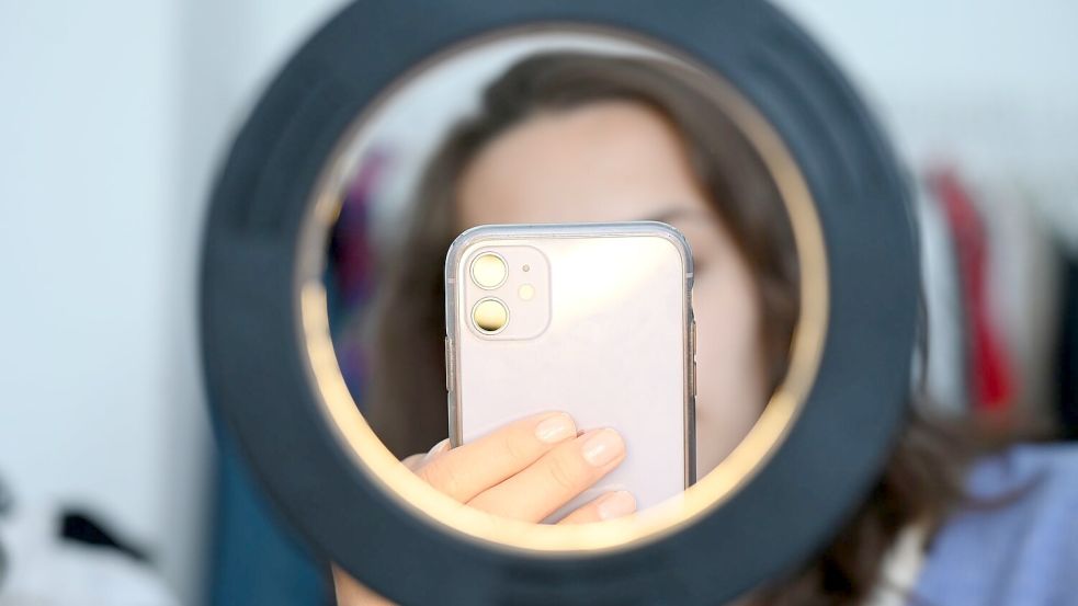 Eine Frau sitzt hinter einem Ringlicht und macht dabei Aufnahmen von sich (Symbolbild) Foto: Niklas Graeber/dpa