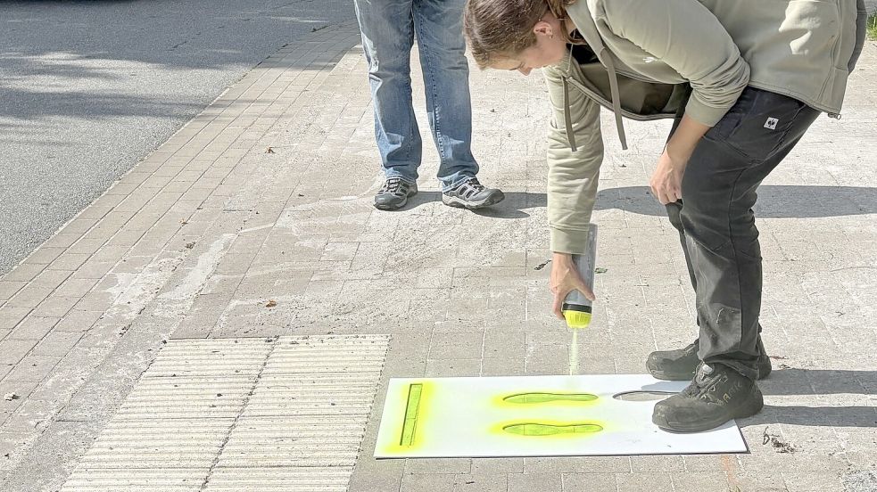 Für die Aktion „Kleine Füße“ sprüht Ramona Janssen mit neongelber Farbe den Abdruck von Kinderfüßen an die Ampel an der Schule. Foto: Mieke Matthes