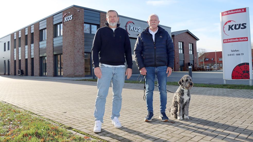 Johannes Bley (rechts) und Juri Breise vor der neuen Halle der KÜS-Prüfstelle in Aurich-Schirum. Mit im Bild: Haus- und Hofhund „Max“. Fotos: Axel Wittich