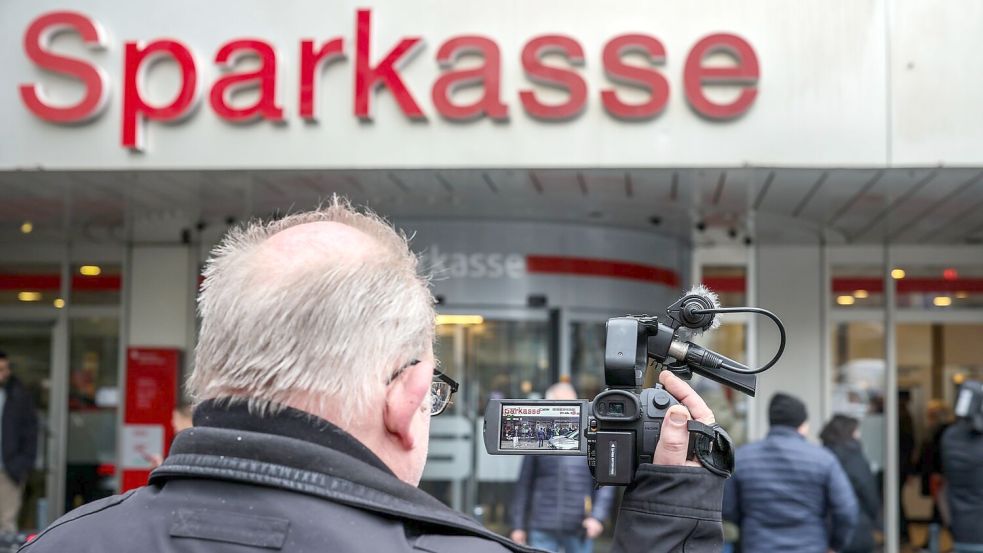 Ein Medienvertreter steht mit einer Kamera vor der Sparkassenfiliale in Buer. Foto: Christoph Reichwein