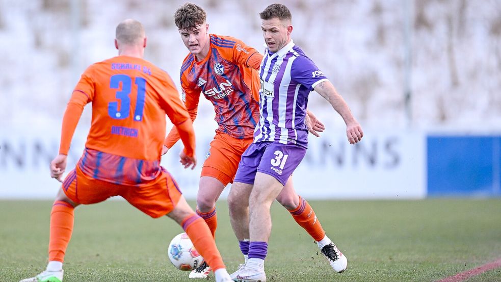 Grüner Rasen, Schnee im Hintergrund: Das Testspiel zwischen dem VfL Osnabrück und Schalke 04 wurde kurzerhand nach Gelsenkirchen verlegt. Hier versucht sich Patrick Kammerbauer (VfL) gegen Tim Dietrich und Dylan Leonard durchzusetzen. Foto: IMAGO/KROEGER/RHR-FOTO