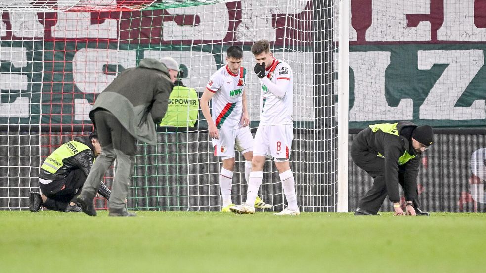 Spieler und Ordner sammeln nach dem Fanprotest Gegenstände vom Rasen. Foto: Harry Langer