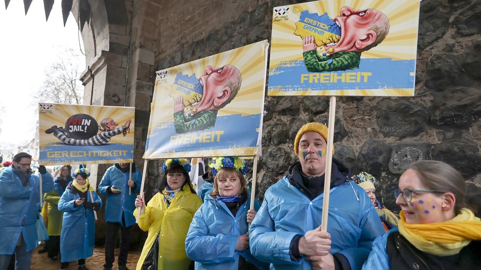 Mitglieder des ukrainischen Hilfsvereins Blau-Gelbes Kreuz halten im Kölner Rosenmontagszug Plakate mit früheren Putin-Darstellungen aus den Zügen in Köln und Düsseldorf hoch. Foto: Oliver Berg