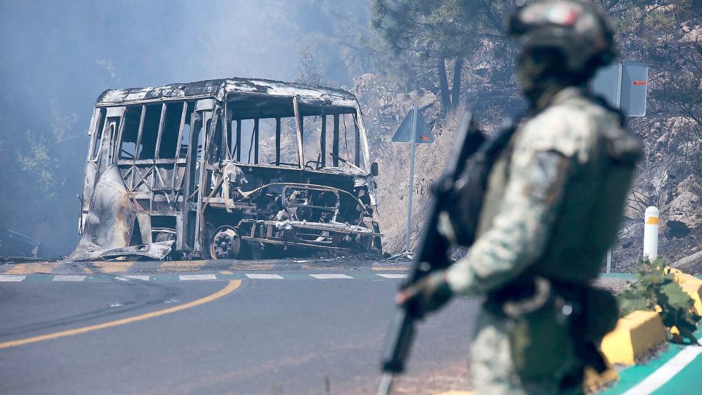 Ein Soldat steht in Mexiko - einem der drei Ausrichterländer der Fußball-WM im Sommer - neben einem ausgebrannten Bus. Foto: Armando Solis/AP/dpa