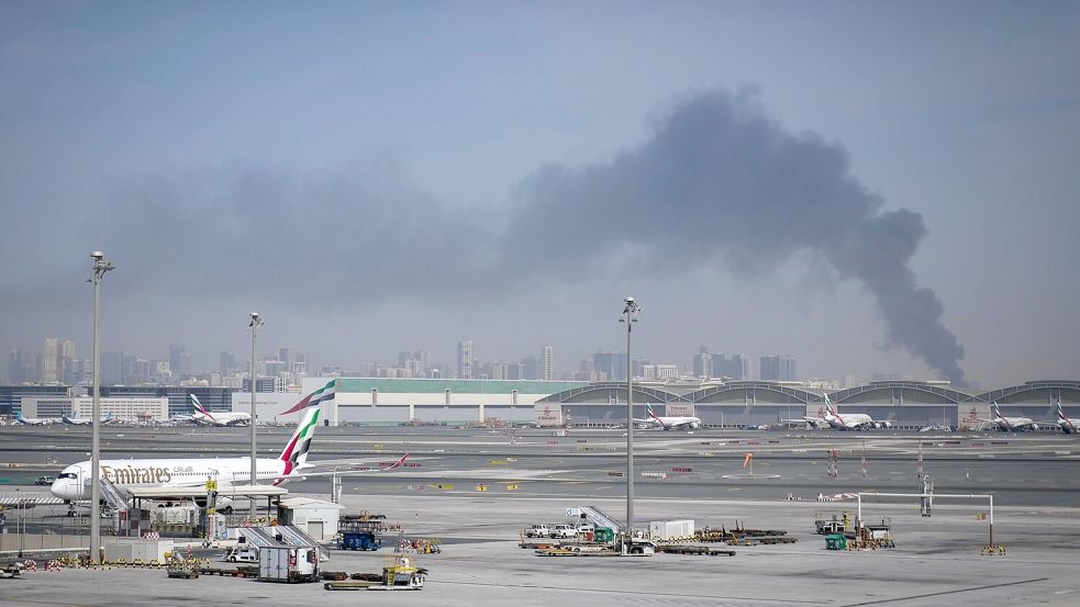 Eine Rauchwolke im Hintergrund, während Flugzeuge auf dem geschlossenen Dubai International Airport geparkt sind. Foto: Altaf Qadri/AP/dpa