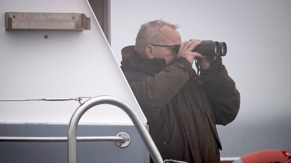 Mecklenburg-Vorpommerns Umweltminister Till Backhaus (SPD) steht mit einem Fernglas auf dem Polizeiboot „Uecker“. Foto: Philip Dulian