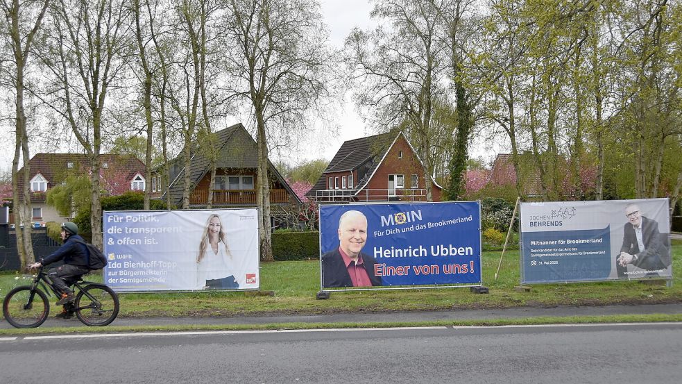Ein Radfahrer passiert Banner, mit denen die Bürgermeisterkandidaten Ida Bienhoff-Topp, Heinrich Ubben und Jochen Behrends an der Rosenstraße in Marienhafe für sich werben. Foto: Thomas Dirks