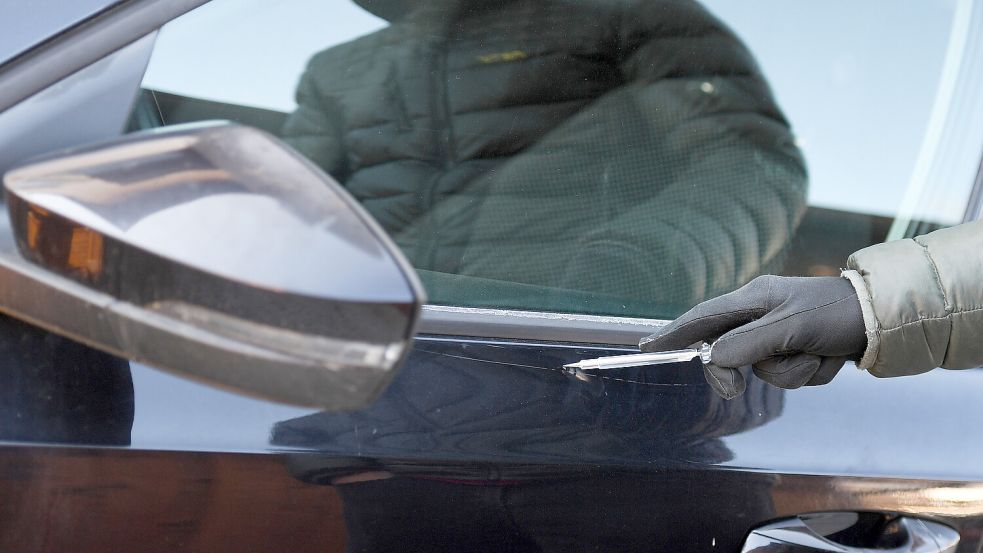 Ein Mann zerkratzt mit einem Schraubendreher den Lack eines Autos. Foto: Angelika Warmuth/DPA