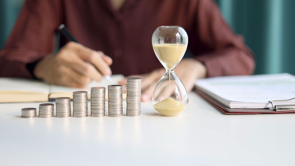 Rising Stapel von Münzen und laufende Sanduhr auf dem Tisch. Steigerung der Einkommens-, Spar- oder Renditeinvestitionen durch Zeit. Zeit- und Geldkonzept. Foto: www.imago-images.de