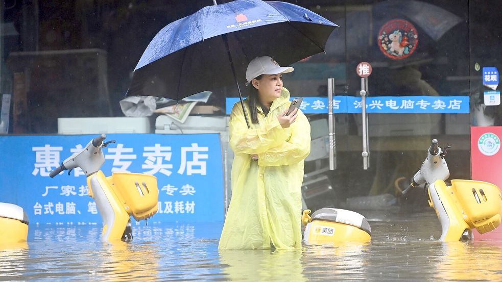 Eine Frau steht in Qinzhou auf einer mit Wasser vollgelaufenen Straße. Foto: Zhang Ailin/XinHua/dpa