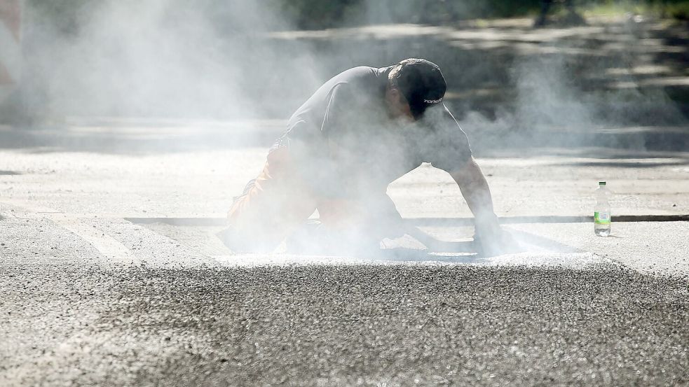 Ein Bauarbeiter repariert eine Straße in Berlin mit Bitumen, einem Bindemittel für Asphalt. (Symbolbild) Foto: Wolfgang Kumm/dpa
