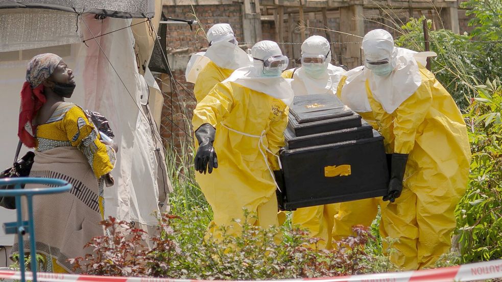 Mitarbeiter des Roten Kreuzes tragen in Schutzanzügen den Sarg einer an Ebola verstorbenen Person aus einem Gesundheitszentrum in Rwampara. Foto: Moses Sawasawa