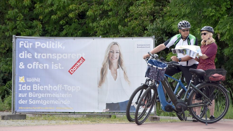 Radtouristen halten vor einem Werbebanner, auf dem Wahlsiegerin Ida Bienhoff-Topp einen „Danke“-Aufkleber für ihre Wähler angebracht hat. Foto: Thomas Dirks