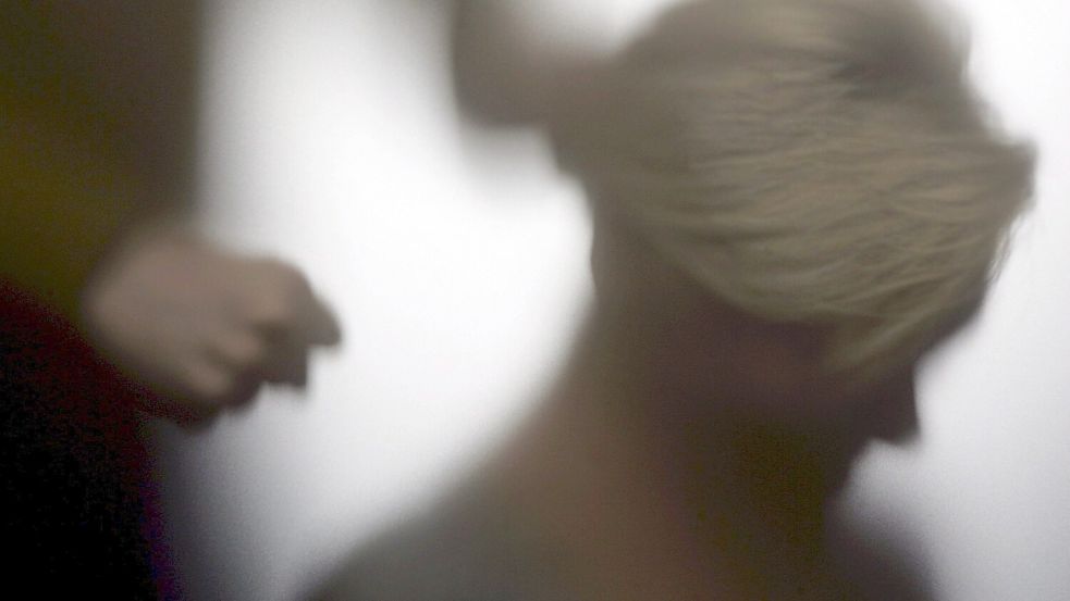 Der Schatten einer Frau wird auf eine Wand projiziert, während im Vordergrund eine Person eine Faust ballt. Foto: DPA