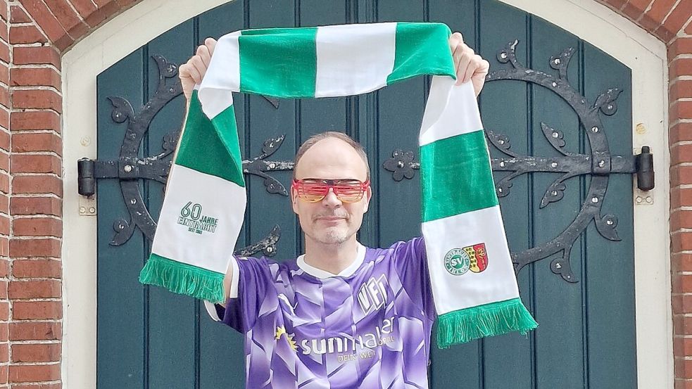 Im Fußballfieber: Pastor Dieter Garlich im Fußballtrikot und mit Schal des SV EIntracht Ihlow vor dem Tor der Kirche in Ihlowerfehn. Foto: Linda Hattensaur