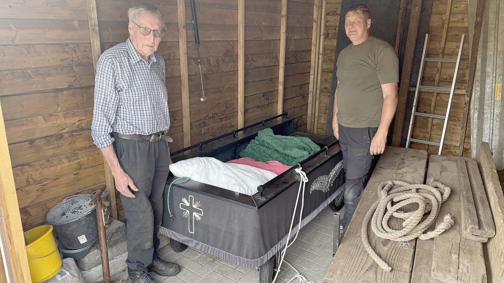 Johann Groenhagen (links) und sein Sohn Alfred Groenhagen, Inhaber der Ihrhover Firma Garten- und Landschaftsbau, stehen bei dem Sargwagen im Schuppen. Den Wagen hat ein Unbekannter wohl zweckentfremdet und darauf geschlafen. Der Einbrecher hatte sogar zwei Kopfkissen mitgebracht. Foto: Carsten Ammermann