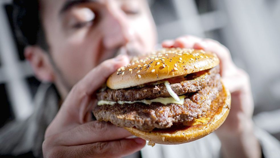 Illustration - Ein Mann beißt in einen Burger Foto: picture alliance/dpa