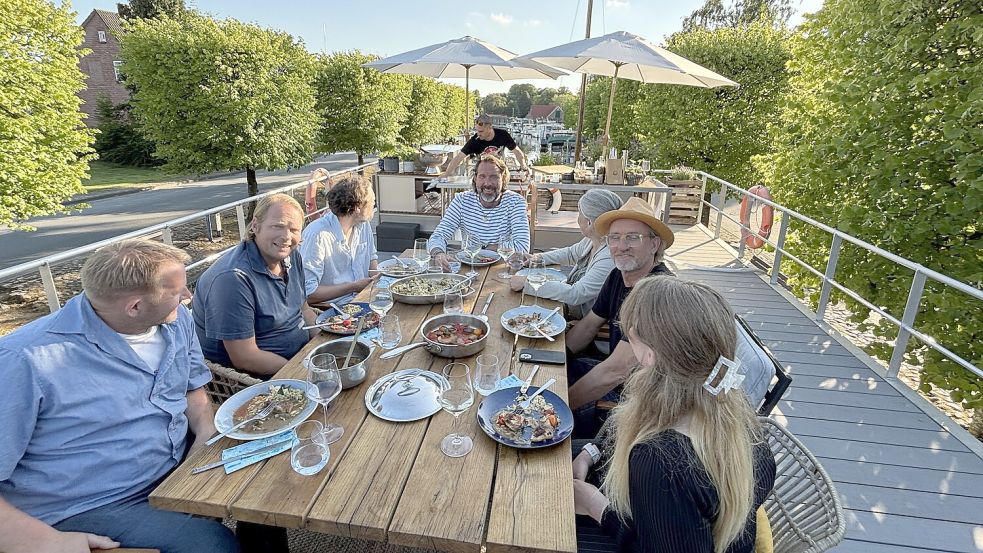 Vier Gäste aus Aurich und Großefehn haben die Spitzenköche Björn Freitag (Zweiter von links) und Frank Buchholz (Zweiter von rechts) unter schöner Abendsonne im Auricher Hafen bewirtet. Mit an der Tafel sitzt Skipper Kai Linnenbrügger (Mitte). Foto: Karin Böhmer