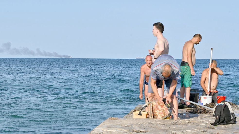 Menschen in Odessa sonnen sich, während am Horizont im Schwarzen Meer der brennende Getreidetransporter „Golden Leo“ zu sehen ist. (Archivbild) Foto: Michael Shtekel