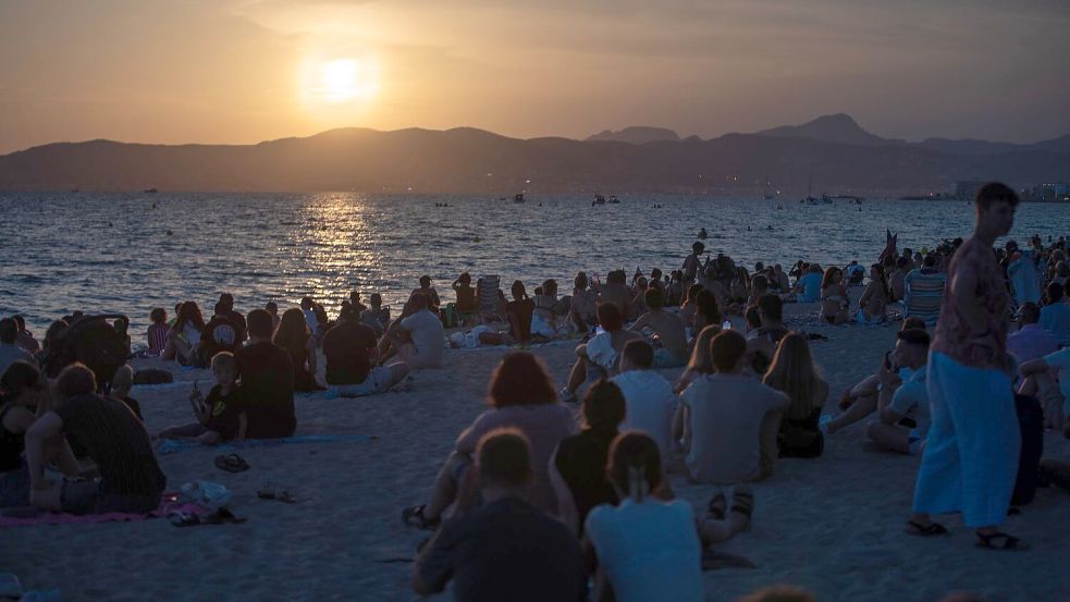 Menschen sitzen am Strand von Palma und warten auf die totale Sonnenfinsternis. Foto: Clara Margais/dpa