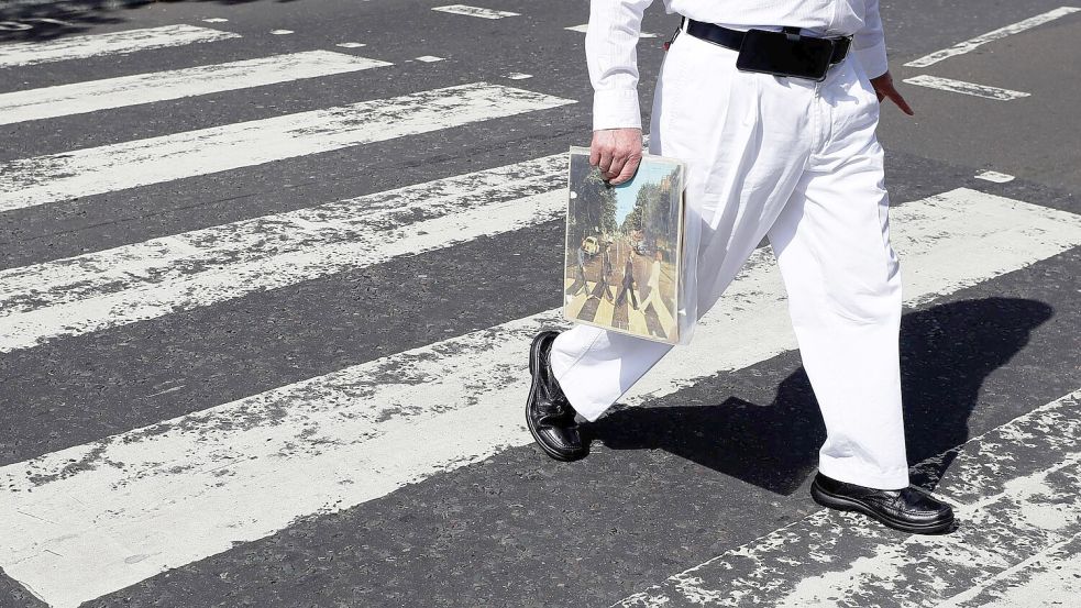 Einer der berühmtesten Zebrastreifen der Welt: Ein Fan trägt eine Ausgabe des Beatles-Albums „Abbey Road“, als er die Abbey Road überquert. (Archivfoto) Foto: Kirsty Wigglesworth/AP/dpa